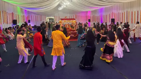 A gathering of people dancing in a room wearing brightly coloured clothing. 