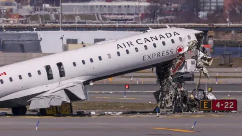 EPA An image showing the Air Canada plane that crashed in LaGuardia post-impact. The plane has the airline's logo on its side. Its front is mangled with its interior contents spilling out.