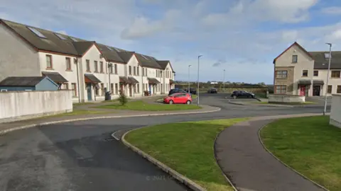 A Google street view of a residential housing estate during the day. Several cars can be seen parked in front of the houses.