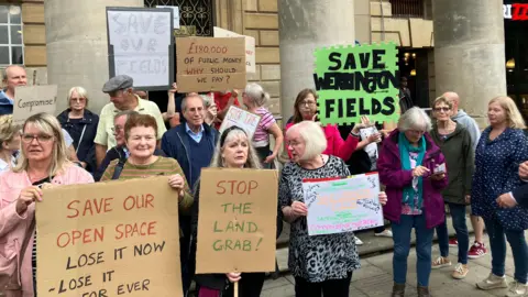 Shariqua Ahmed/BBC Protesters holding signs that read "Save our open space" and "Stop the land grab" 