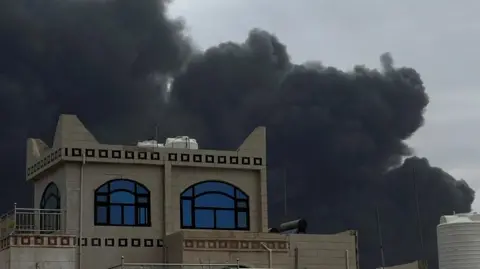 A black cloud of smoke hovers above a building with blue windows