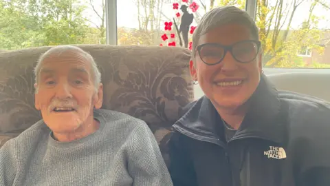 An image of Thomas Woodruff and his daughter Helen Halliwell, both are smiling. He is wearing a grey jumper while she is wearing a black North Face jacket and black glasses.