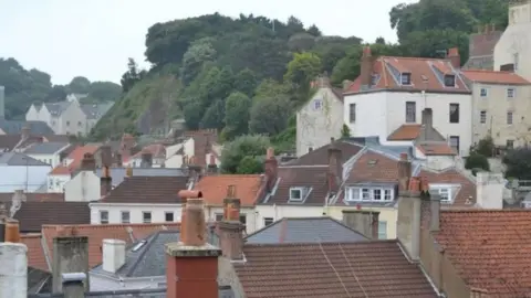 BBC The red-tiled rooftops of houses in Guernsey set against a backdrop of trees and hedges