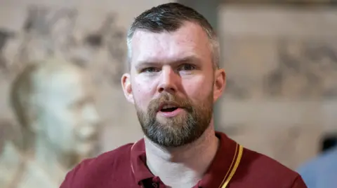 PA Media Gerry Carroll -  a greying haired man with a beard wears a maroon polo shirt