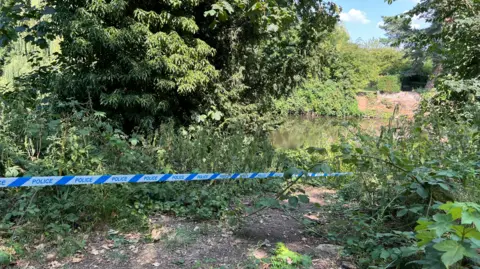 BBC Police tape around a small path leading to the River Derwent in Derby. 