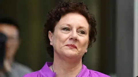Kathleen Folbigg wearing a purple shirt. She has short curly brown hair.