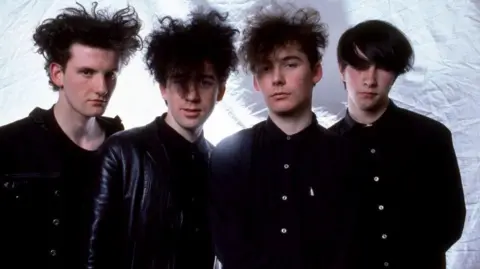 Getty Images Jesus and Mary Chain. Four men wearing all black. Three of them have backcombed dark hair while the fourth has his dark hair swept over his face, obscuring his eyes 