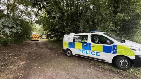 Martin Giles/BBC Police vehicles parked along a dirt track. One is pointing away from the camera while the second one, in the foreground, is parked diagonally. 