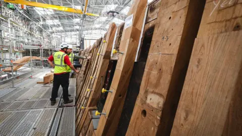 Getty Images Men in high vis jackets looking at timber that is set up in a warehouse