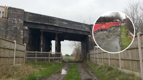 A bridge crossing over a dismantled railway line with wooden fences leading to it on both sides. A circle with a picture of cracks in the road is also shown. 