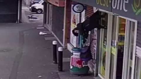 CCTV shows a woman hoisted into the air due to her coat becoming stuck in shop shutters