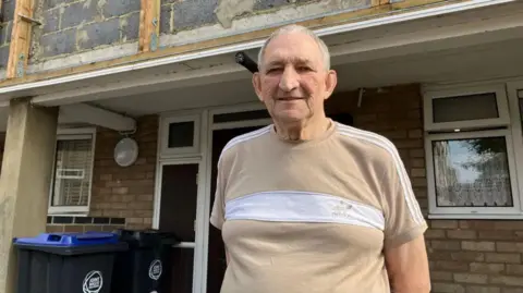 Middle-aged man in t-shirt standing outside the front of his flat on an estate