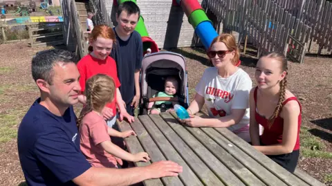 The Wilson family sit at a picnic table beside a children's play area at Mountpanther Farm Park in County Down.