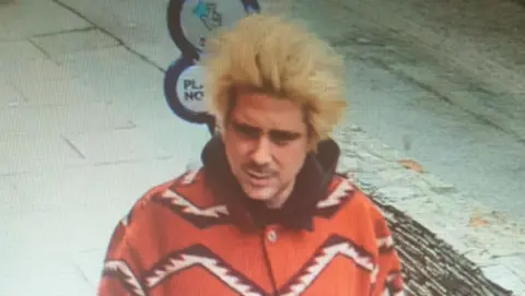 CCTV image showing Alexander Key wearing an orangey red overshirt with white zig-zag lines on it.