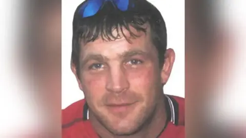 GMP A young Paul Quinn wearing a red t-shirt with sunglasses on his head smiles. 