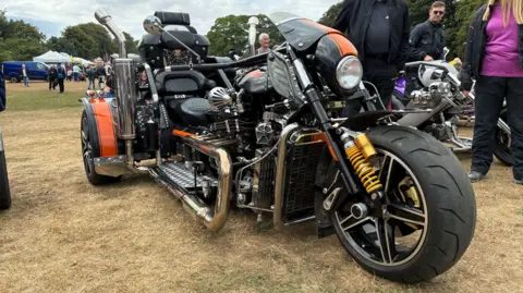 A large, three-wheeled, black motorcycle parked on a grass field. 