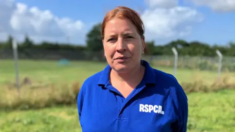 Suzanne Norbury stood in a field, looking straight ahead. She can be seen from the chest up and is wearing a blue polo shirt with 'RSPCA' on it. She has a neutral expression.