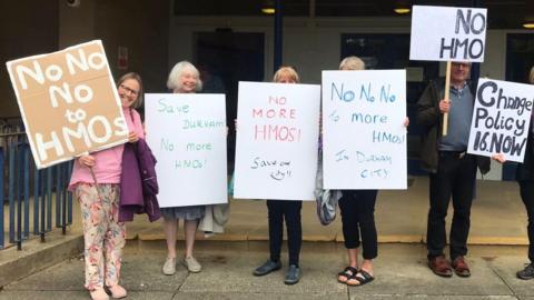 A group of men and women holding placards with anti-HMO wording