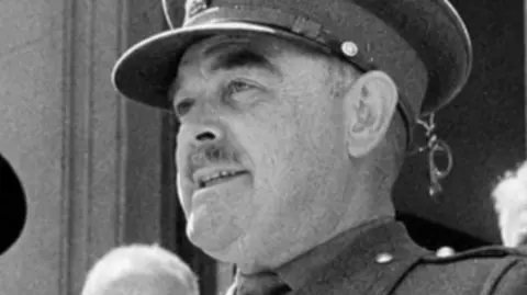In a black and white image, Brig Snow is standing in full military uniform and looking away from the camera