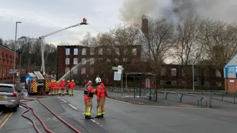 Carl Haslam/GMFRS Smoke rise after the fire crews extinguish the blaze in the building. Fire engine and crew members can be seen on the road.