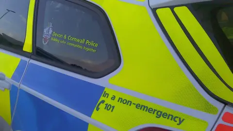 A picture of the side of a blue, yellow and white police car. The logo for the police force is on the window and the contact details is below.