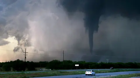 A tornado almost touching the ground with a road in the foreground.