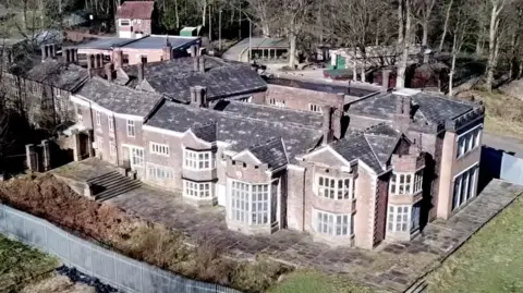 Hopwood Productions An aerial shot of Hopwood Hall in Middleton, Rochdale. It is a large manor house surrounded by a metal fence and countryside. 