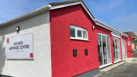 RHT The Rushen heritage Centre, which painted white with a red front. It has large glass windows and a glass door.