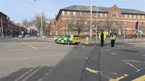 BBC Two police officers standing outside a cordon with a police vehicle at the scene