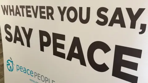 A white board with the words 'WHATEVER YOU SAY, SAY PEACE' printed on it. 