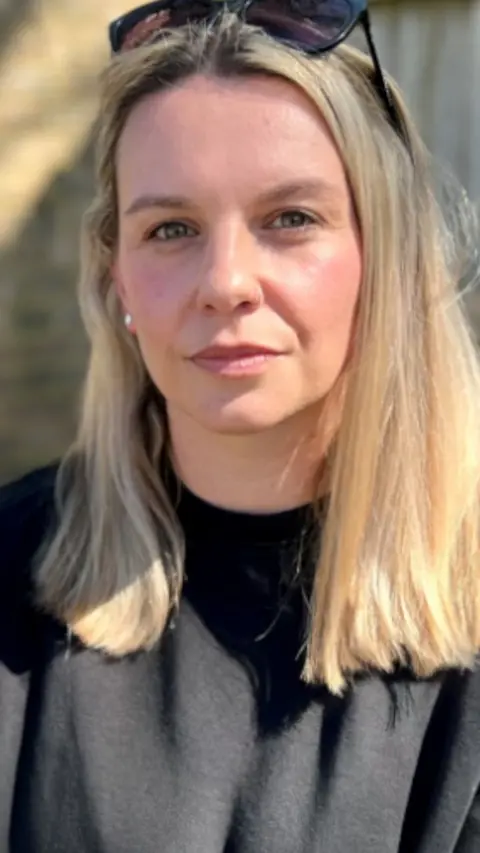 Rachel Moore looks at the camera. She has shoulder length blonde hair with a pair of black sunglasses on top of her head and wears a black cotton t shirt.