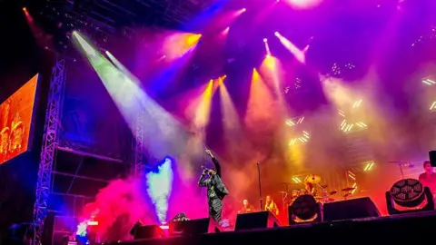 Getty Images Faithless performing on a stage with multi-coloured lights and smoke.