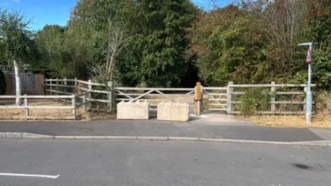 Two large concrete blocks are pictured in front of a gate, which leads into a field.