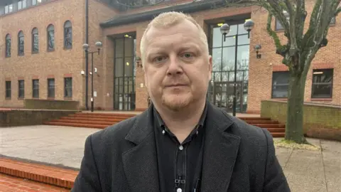 BBC A man in black clothing stood in front of Derby Crown Court