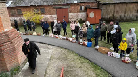 People line up with easter baskets outside a church.