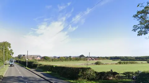 A view of Winchester Road and the open fields to its east, with the edge of Blaby peeping over hedges in the background