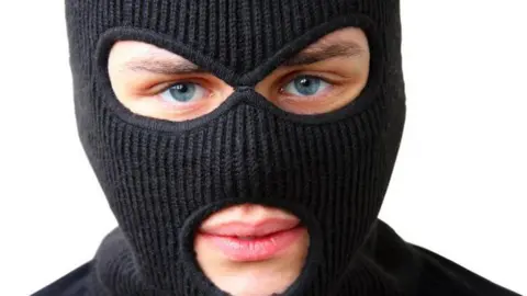 A man wearing a black balaclava. Only his lips and eyes are visible.
