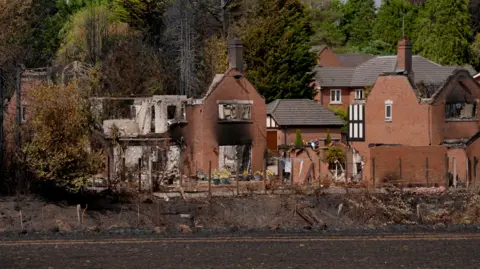 PA Media A burnt out house in Stourbridge, which has lost its roof and most of its walls, next to a burnt but not destroyed property. Charred grass is visible in front of the houses.