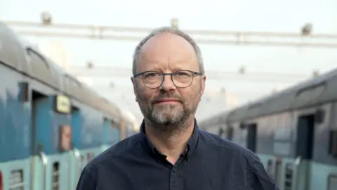 Robert Llewellyn pictured in between two trains when filiming 'The World's Busiest Railway 2015' in Mumbai.