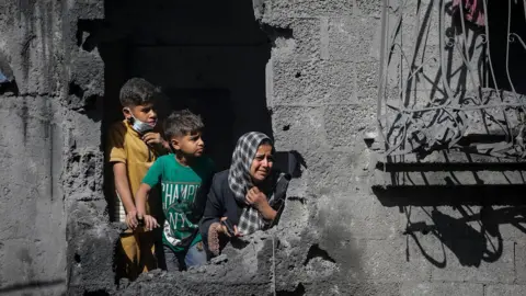 EPA Palestinians look out from their family's home following an Israeli air strike on a residential block in al-Shati refugee camp, northern Gaza (29 October 2025)