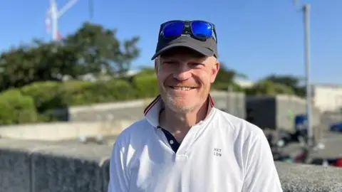 Smiling man with fair complexion in white polo shirt and baseball cap