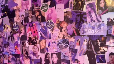 A wall, lit with a purple light and covered in photos of young people and hearts