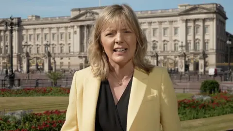 Ellie Price wearing yellow blazer, reports from outside Buckingham Palace