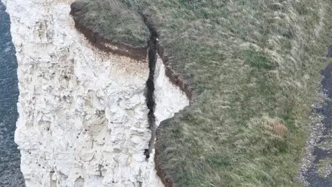 An aerial view of the cliff shows a long, deep crack in the cliff face