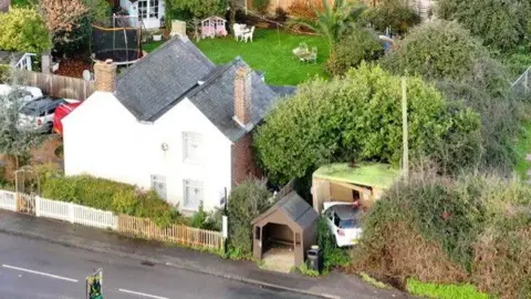 Eddie Mitchell A drone image of the site where a car crashed into a gas substation near Nyetimber, West Sussex. A white car can be seen crashed into the substation building, which is just beside a brown bus stop.