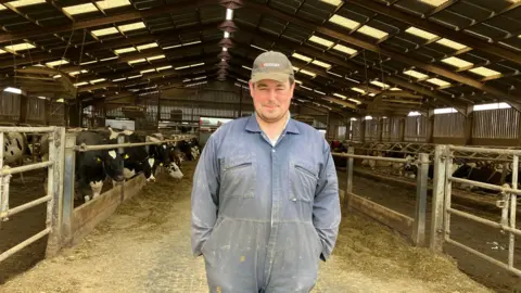 a farmer dressed in overalls standing in a cow barn 