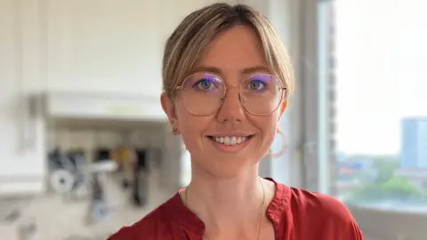 Antonia Jennings, a young woman with round glasses and a red top, smiling at the camera