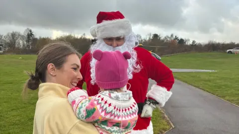 Handout Jo and her daughter Willow, aged 16 months, meet Santa. They are standing outside. 