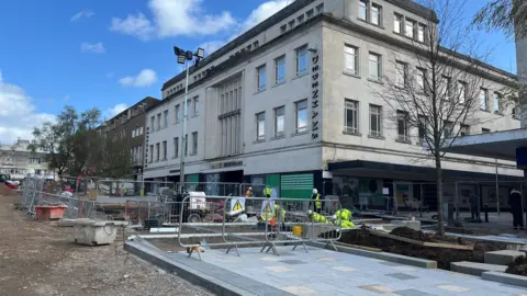 Metal barricades and new paving stones on New George Street in Plymouth with workmen in the background