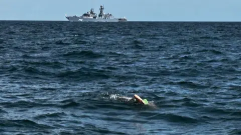 Sheppey Channel Champions A swimmer in a green swim hat in the Channel with a grey warship in the background